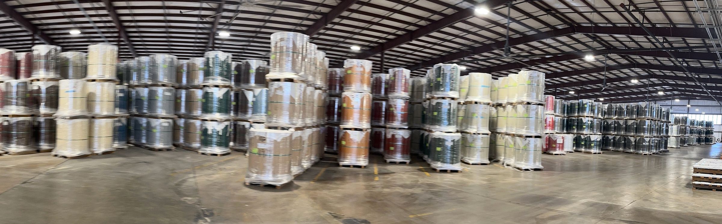 Rows of shrink-wrapped painted steel coils stacked on pallets in a supplier's warehouse